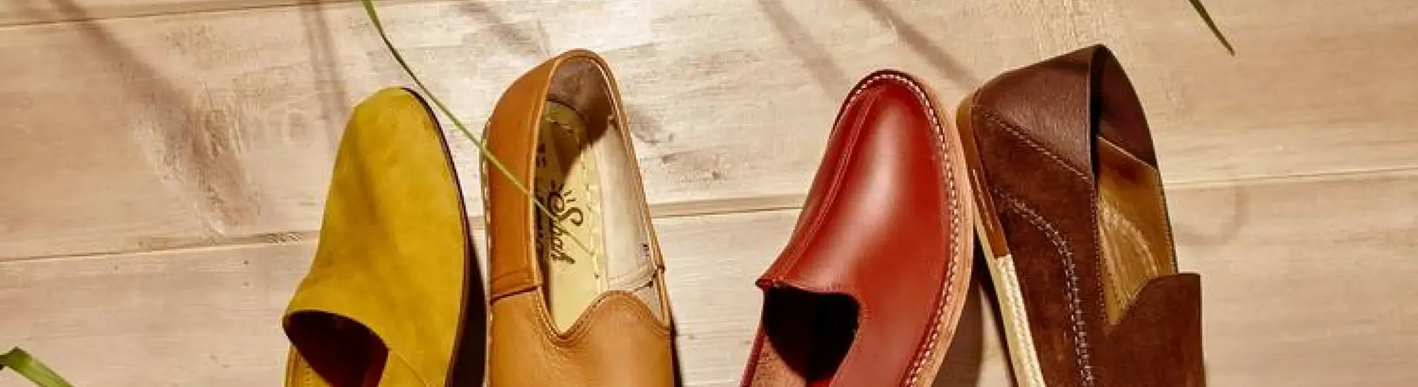 Row of mustard, tan, red and brown leather slip-on shoes against light wooden boards