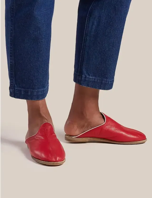 Close-up of feet wearing red leather slip-on mules below cuffed blue jeans
